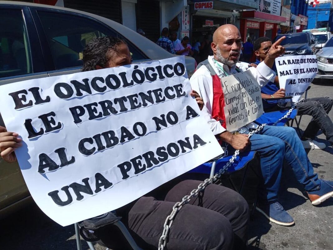 Pastor evangélico se encadena frente al Oncológico del Cibao, RD, en medio de protestas por crisis en dicha entidad pública
